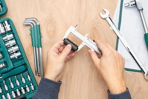 Man measuring object using calliper. Workshop table with many tools. Wrench.. Foto stock