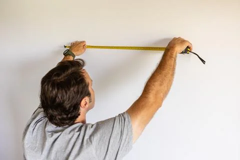 Man measuring white wall for home repair project Stock Photos