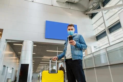 Man in medical face mask using smartphone in airport. Urban traveler wearing Stock Photos