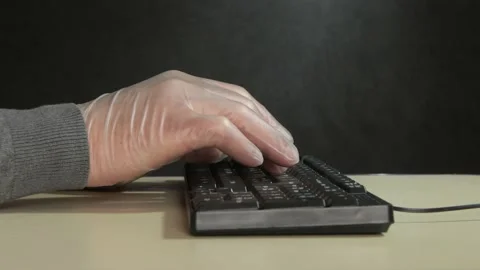 A man in medical gloves is typing on a computer keyboard on a dark background, c Stock Footage 219326342