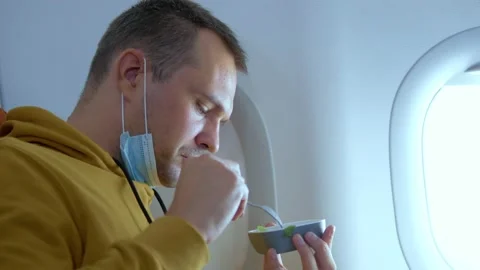 Man in a medical mask eats while sitting in an airplane Stock Footage 140751314