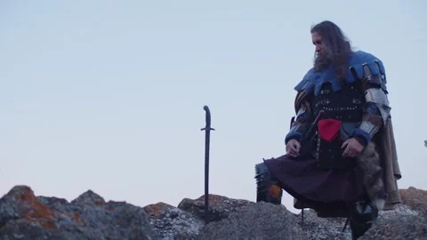 A man in a medieval knight costume pulls a sword from a stone against the Stock Footage 275852853