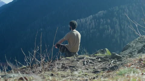 Man Meditating on Log in Mountain Clearing with Forested Mountains Stock Footage 316417834