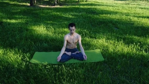 Man is meditating. Professional yoga practicing in park. Handsome bare-chested Stock Footage 77498850