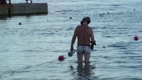 Man with a metal detector looking for lost jewels in the water Stock Footage 79782915