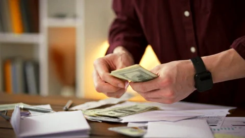 Man meticulously counts stacks of cash on cluttered table immersed in work e Stock Footage 338187358
