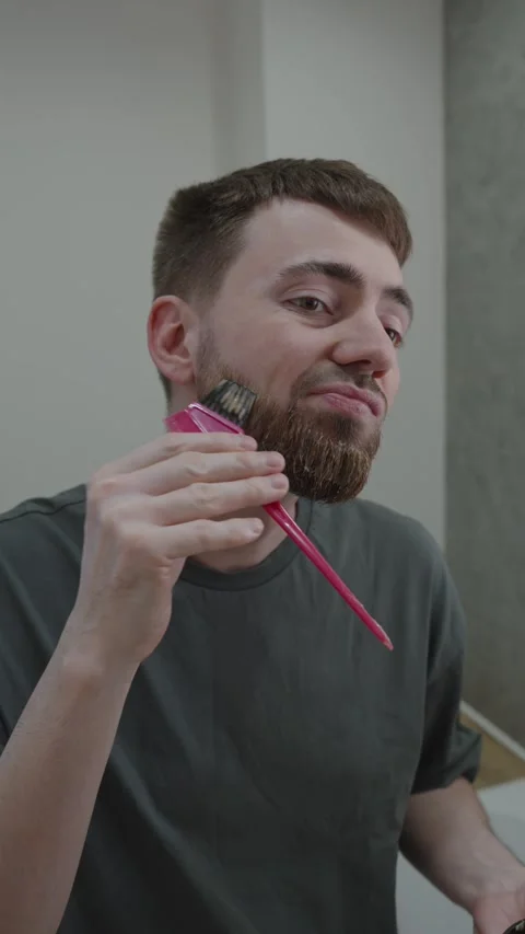 Man meticulously dyes his beard using comprehensive technique 動画素材 333332396
