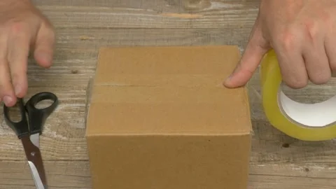 A man is meticulously using tape to carefully seal a cardboard box for shipping Vidéo 279897920