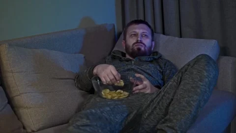 Man Mindlessly Watching Television and Eating Snacks Alone at Night 動画素材 342353124