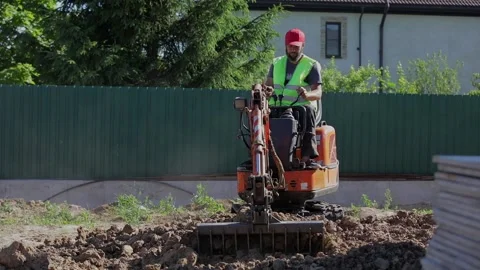 A man on a mini-excavator levels a piece of land, loosens the soil Stock Footage 207863523