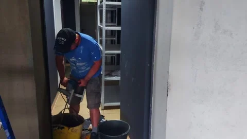 Man mixes plaster with a drill in a building room, wearing a blue shirt and a ca Stock Footage 326962797