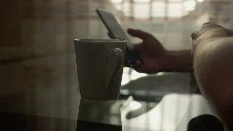 A man with a mobile phone is sitting at a table with a mug of hot coffee Stock Footage 134883301