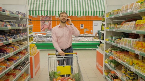 Man with mobile pushing trolley along supermarket grocery aisle Stock Footage 63372438