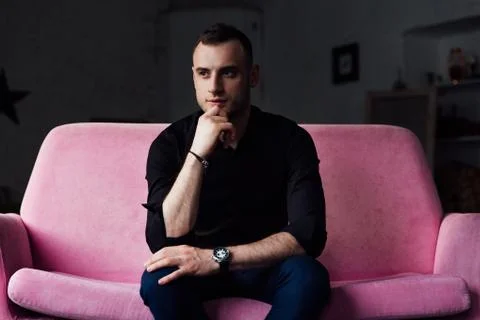 Man model sits on pink sofa in loft interior. Businessman in a black shirt and Stock Photos