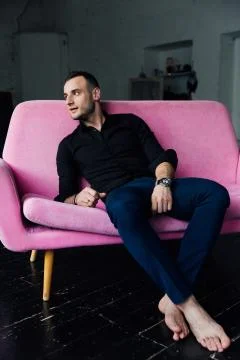 Man model sits on pink sofa in loft interior. Businessman in a black shirt and Stock Photos