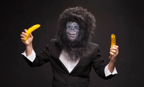 A man in a monkey mask on a black background with two bananas. Stock Photos