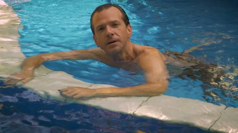 A man motions to the camera to join him in the swimming pool Stock Footage 55448585