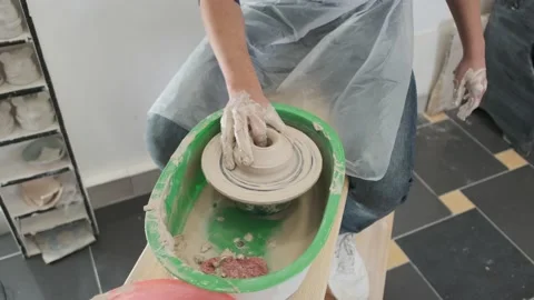 Man is moulding a ware in the pottery studio and the woman is helping him Stock Footage 130875284