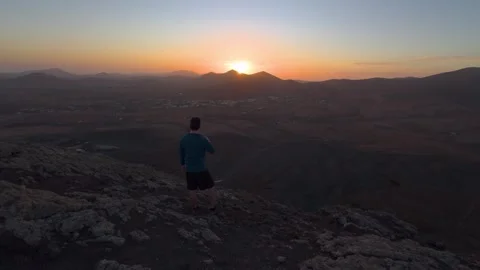 Man on Mountain Ridge at Sunset Over Volcanic Landscape 動画素材 331263447