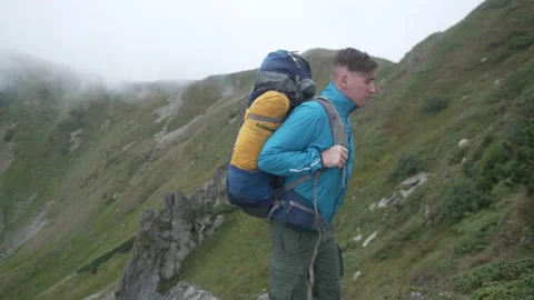 Man in the mountains puts on his backpack and continues walking. Cloudy weather Stock Footage 217395618
