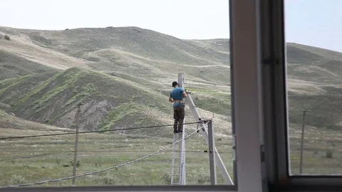 A man mounts electricity on a pole against a background of hills Stock Footage 79407322