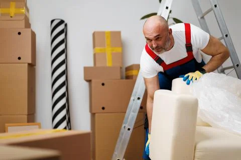 Man mover in uniiform packing sofa for relocation Stock Photos