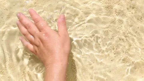 A man moves his hand in the water on a sea, sandy beach. ASMR Stock Footage 246768980