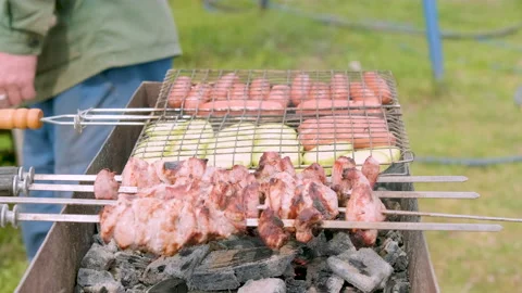 Man moving grill on open air. shashlik sausages and zucchini on a barbecue grill Stock Footage 201533332