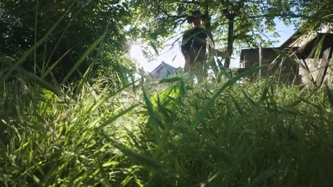 Man mowing grass with electric trimmer from ground level in slow motion backl Stock Footage 340143018