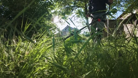 Man mowing grass with electric trimmer from ground level in slow motion backl Stock Footage 340143261