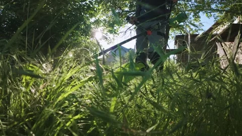 Man mowing grass with electric trimmer from ground level in slow motion backl Stock Footage 340143274