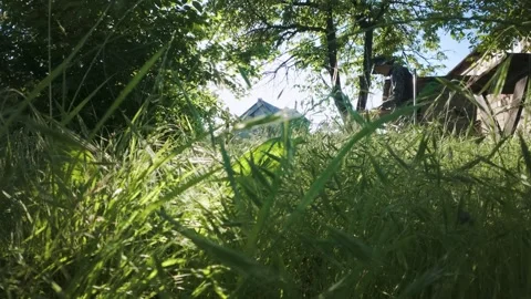 Man mowing grass with electric trimmer from ground level in slow motion backl Stock Footage 340143399