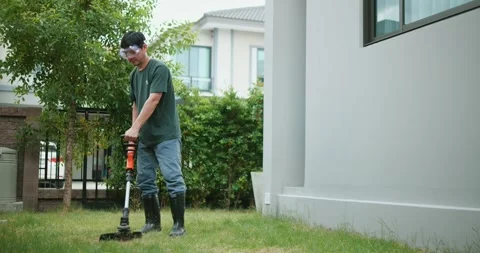 A man mows grass in backyard, with an electric lawn mower. Gardener mowing lawn. Stock Footage 249928969