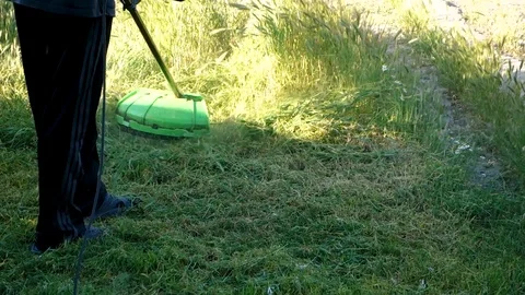 A man mows grass with a hand-held lawn mower outdoors. The gardener works in the Video stock 118751529