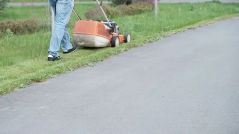 Man mows the lawn with a lawn mower in the park Stock Footage