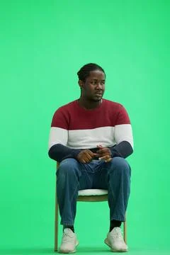 A man in a multi-colored jacket with a backpack on a green background sits on a Stock Photos