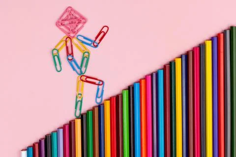 Man from multi-colored paper clips goes up the stairs from multi-colored penc Stock Photos
