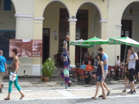 Man in multicolored clothes and on stilts walks in the Havana's square an Vídeos de archivo 71035002