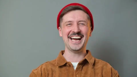 A man with a mustache and beard smiles while wearing a red beanie in a studio Vidéo 337642584