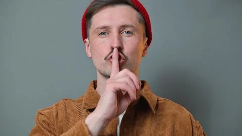 A man with a mustache and red beanie engages in a shushing gesture in front of a Video stock 337642753