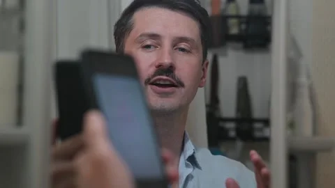 A man with a mustache engages with a smartphone while smiling and gesturing in Stock Footage 337111802