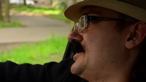 Man with mustache in hat, glasses sitting in car and sing. Summer day. Parody Vidéo 75313776
