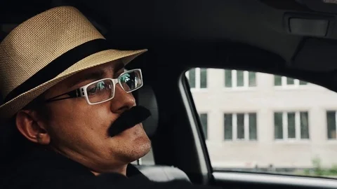 Man with mustache in hat, glasses sitting in car at window and sing. Parody Vidéo 75313952