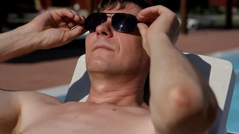 Man with a naked torso lying on the sun chairs and closes his eyes black glasses Stock Footage 103301687