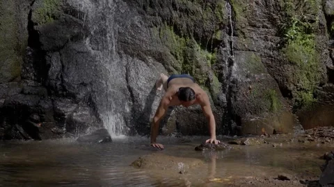 A man, with a naked torso, training in a waterfall, does push-ups in the water Stock Footage 244749023