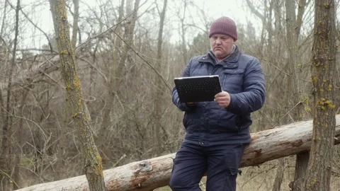 A man in nature looking at his tablet while sitting on a fallen pine tree 스톡 동영상 170982785
