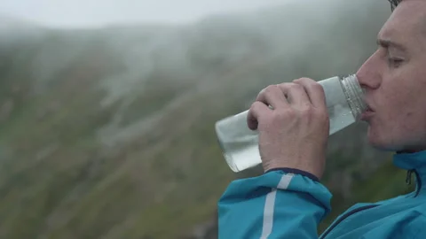 A man in nature opens a bottle of clean water and drinks, among the mountains Stock Footage 240234091