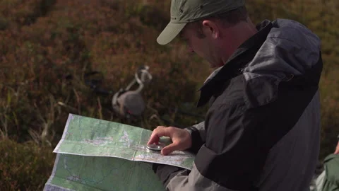 A man navigates the terrain using a map and compass during a mountain hike Stock Footage 140608541