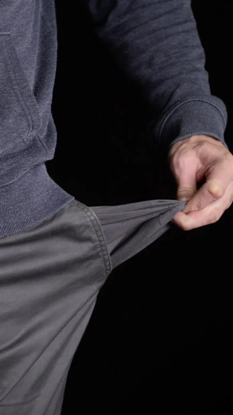 Man in navy hoodie pulls empty gray pants pocket against black background Stock Footage 341834908