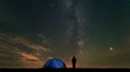 The man near a camping tent standing on stars background. time lapse 4k or 4k+ Resolution